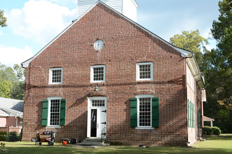 Close view of the brick front gable with a round window, green shutters and a white door