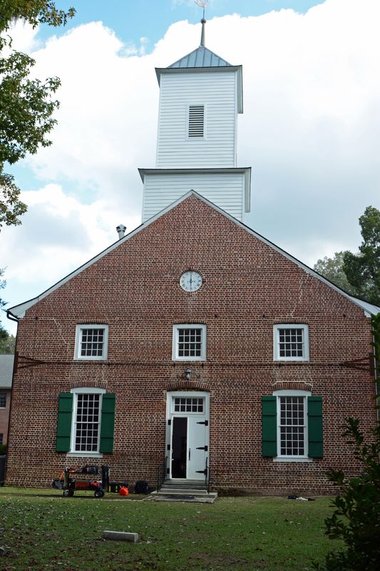 Front gable of the church with a small clock, green shutters and the white steeple above